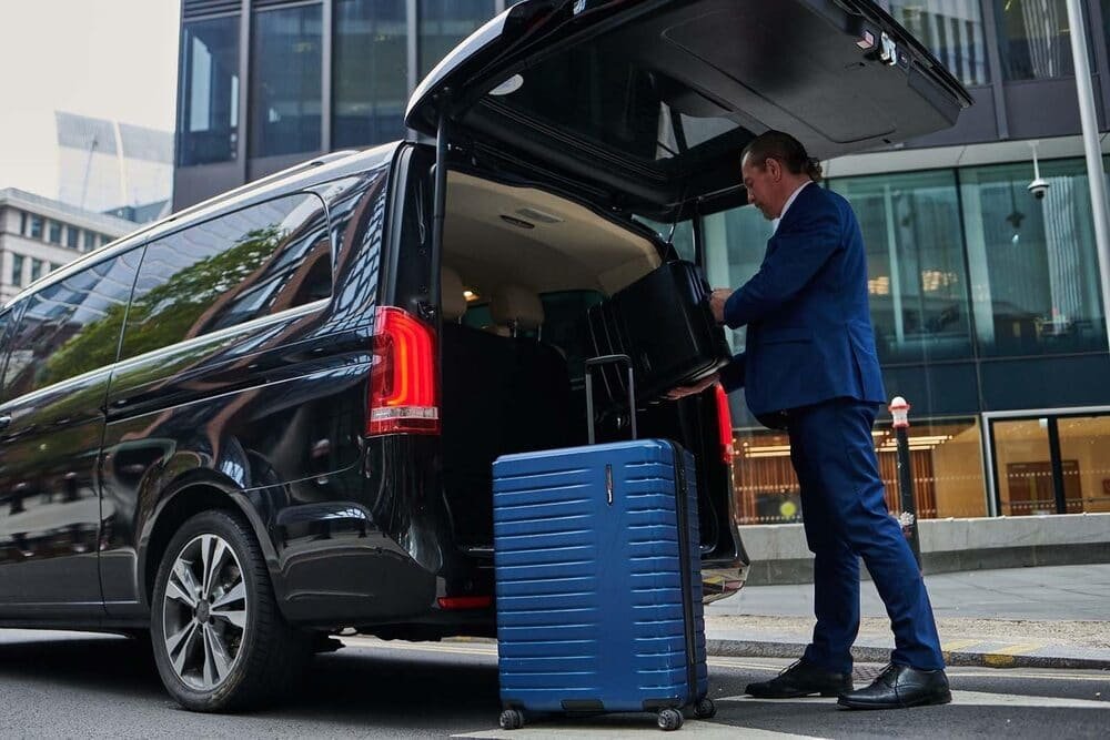 Driver in a suit loading a suitcase into a black people carrier