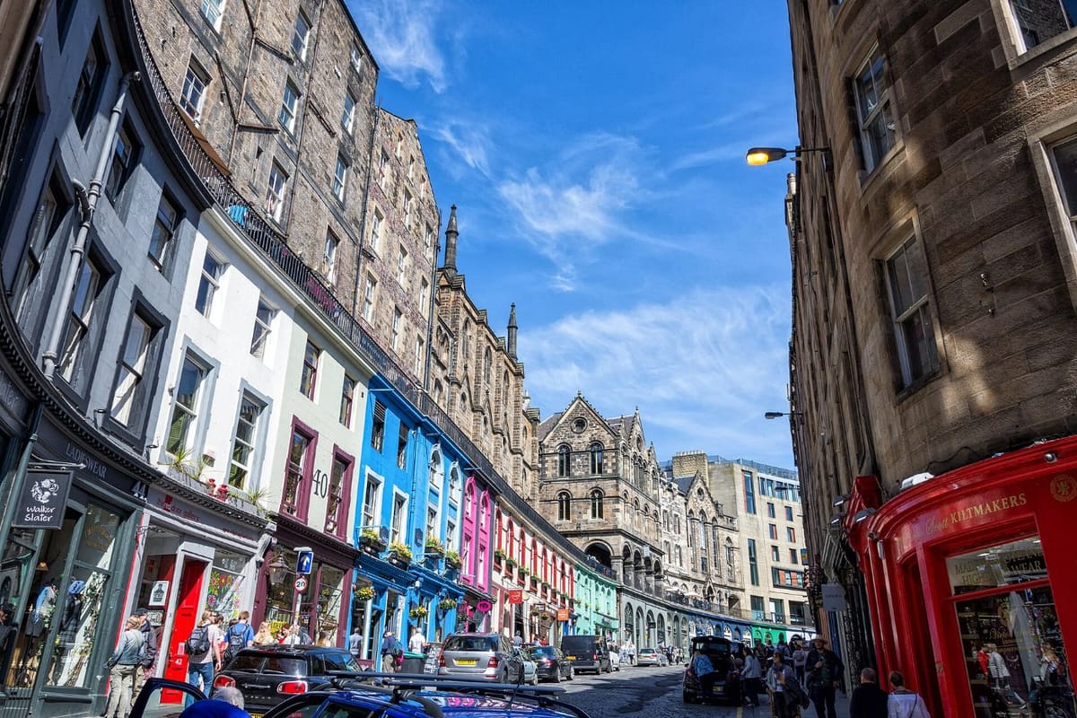 Colourful shopfronts curving down Victoria Street in Edinburgh Old Town under a blue sky